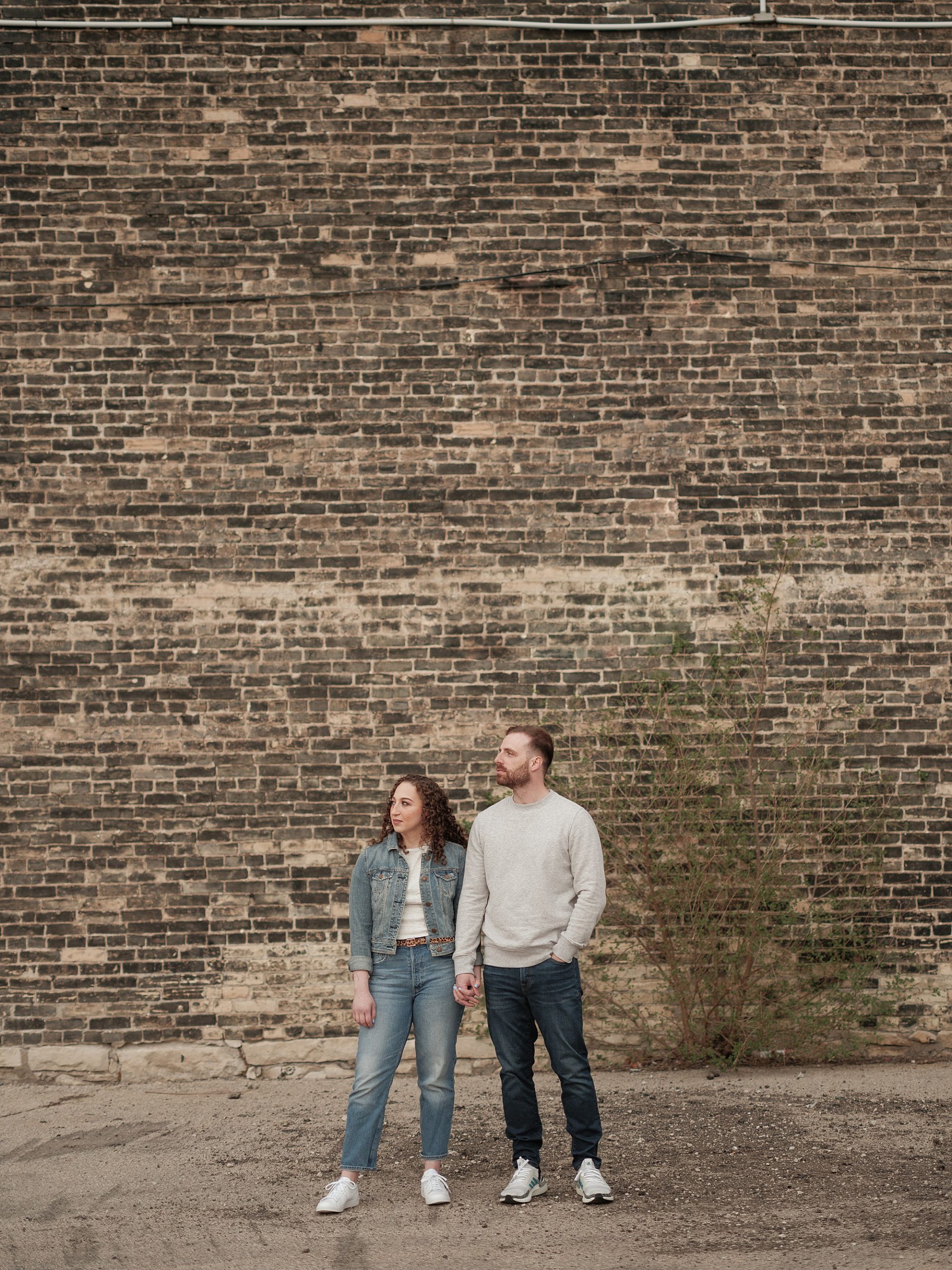 cool couple stands in front of cream city brick