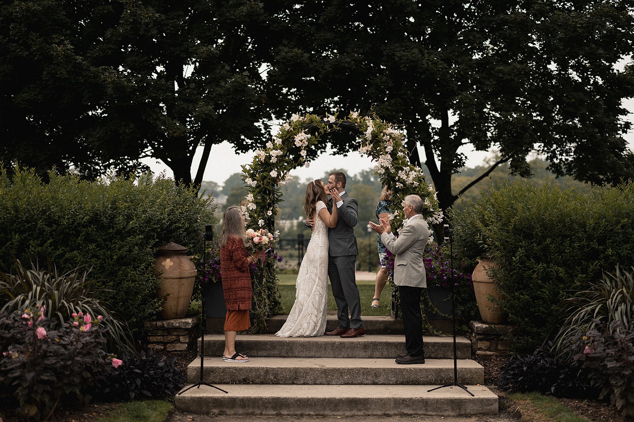 Bride & groom kiss in garden ceremony with two people and judge